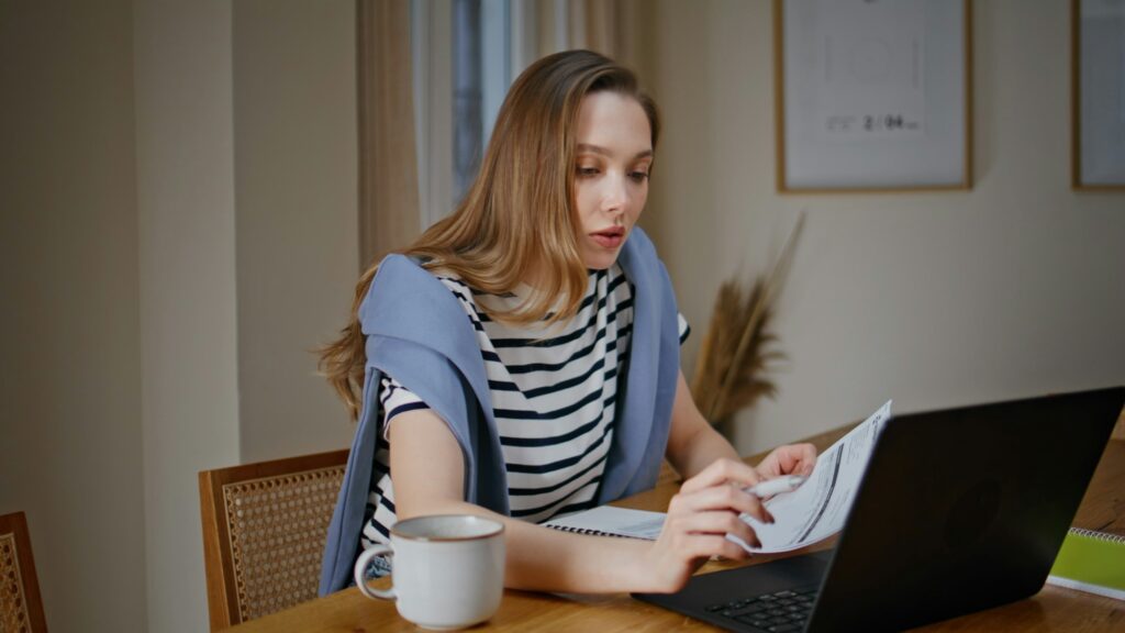 Girl entrepreneur making research on laptop noting information at home closeup